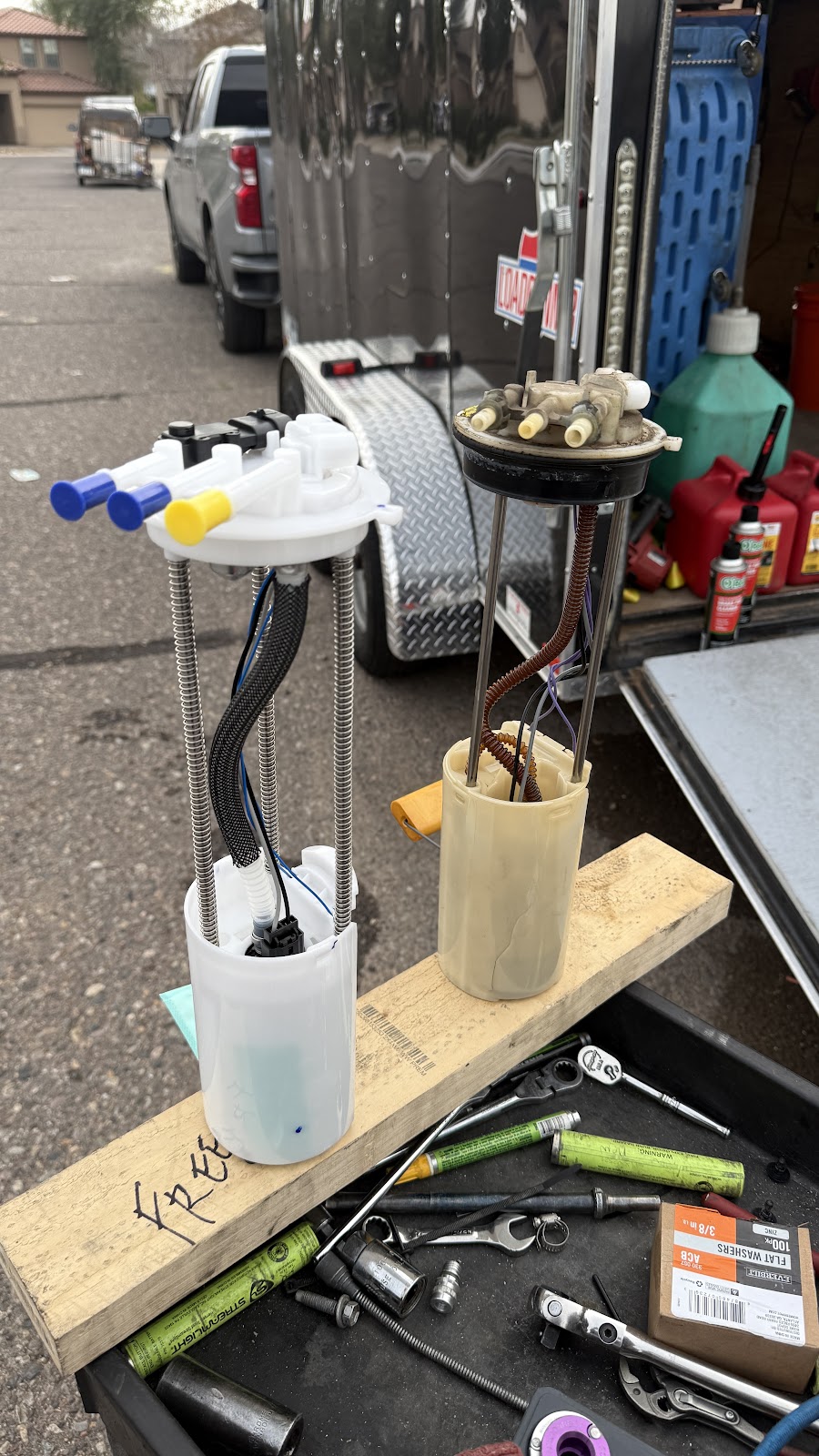 Old and new fuel pump modules standing side by side on a board next to the work trailer