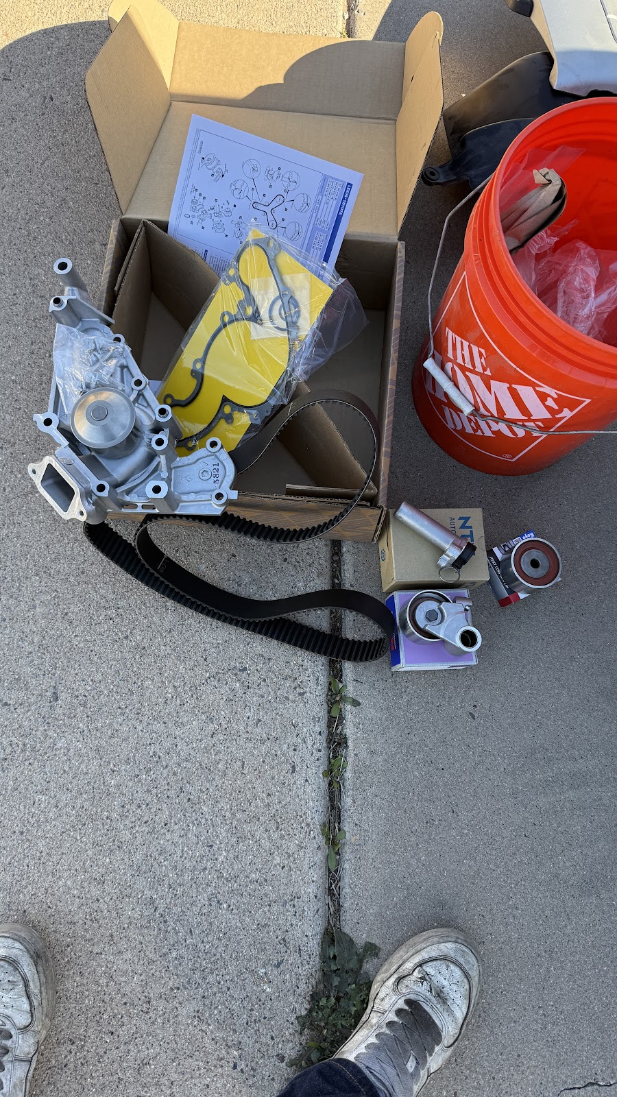 New water pump, timing belt, gaskets and tensioners laid out of the box on a driveway