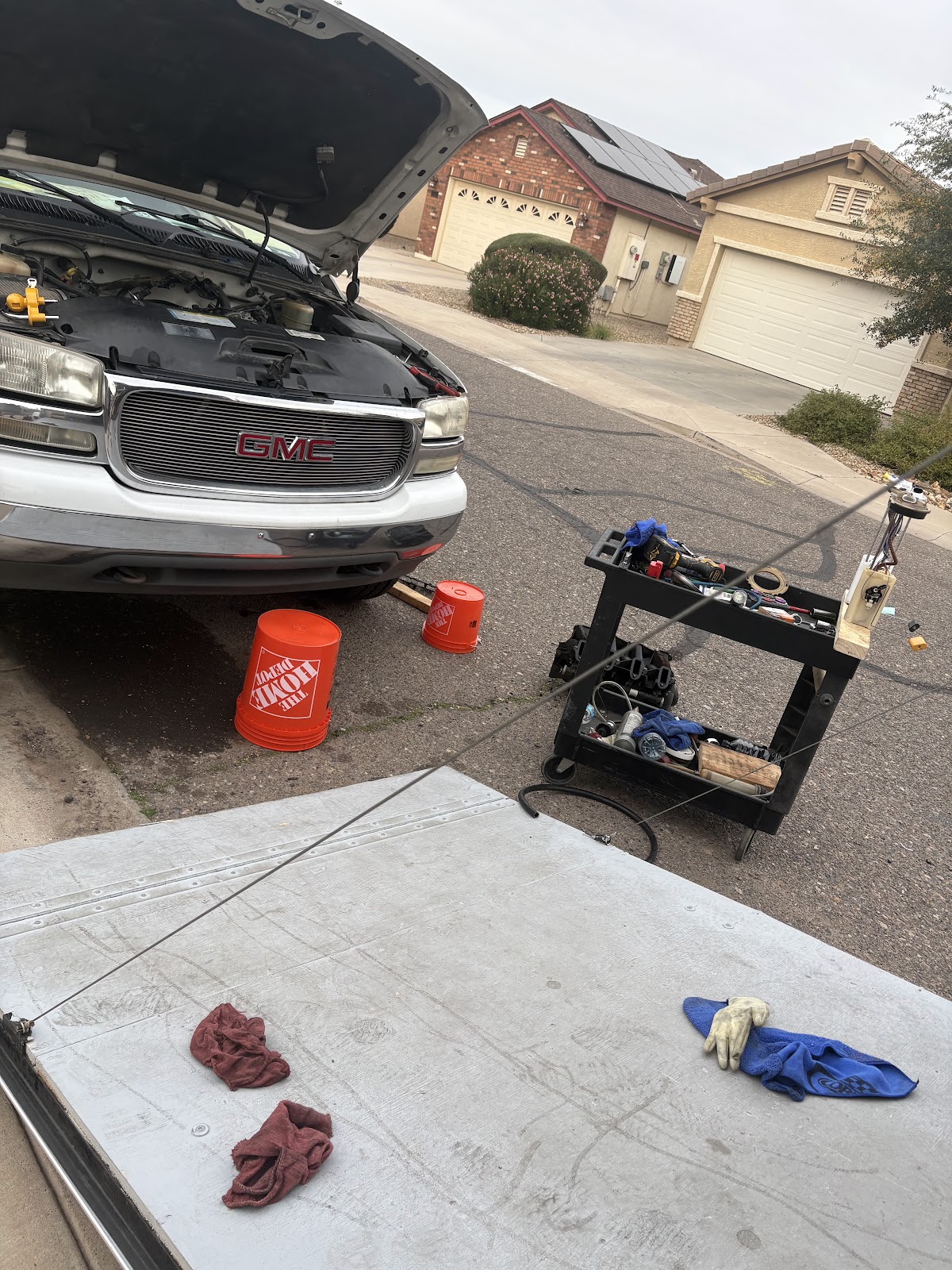 Pickup truck with its hood up at the curb of a Phoenix street, rolling tool cart set up beside it