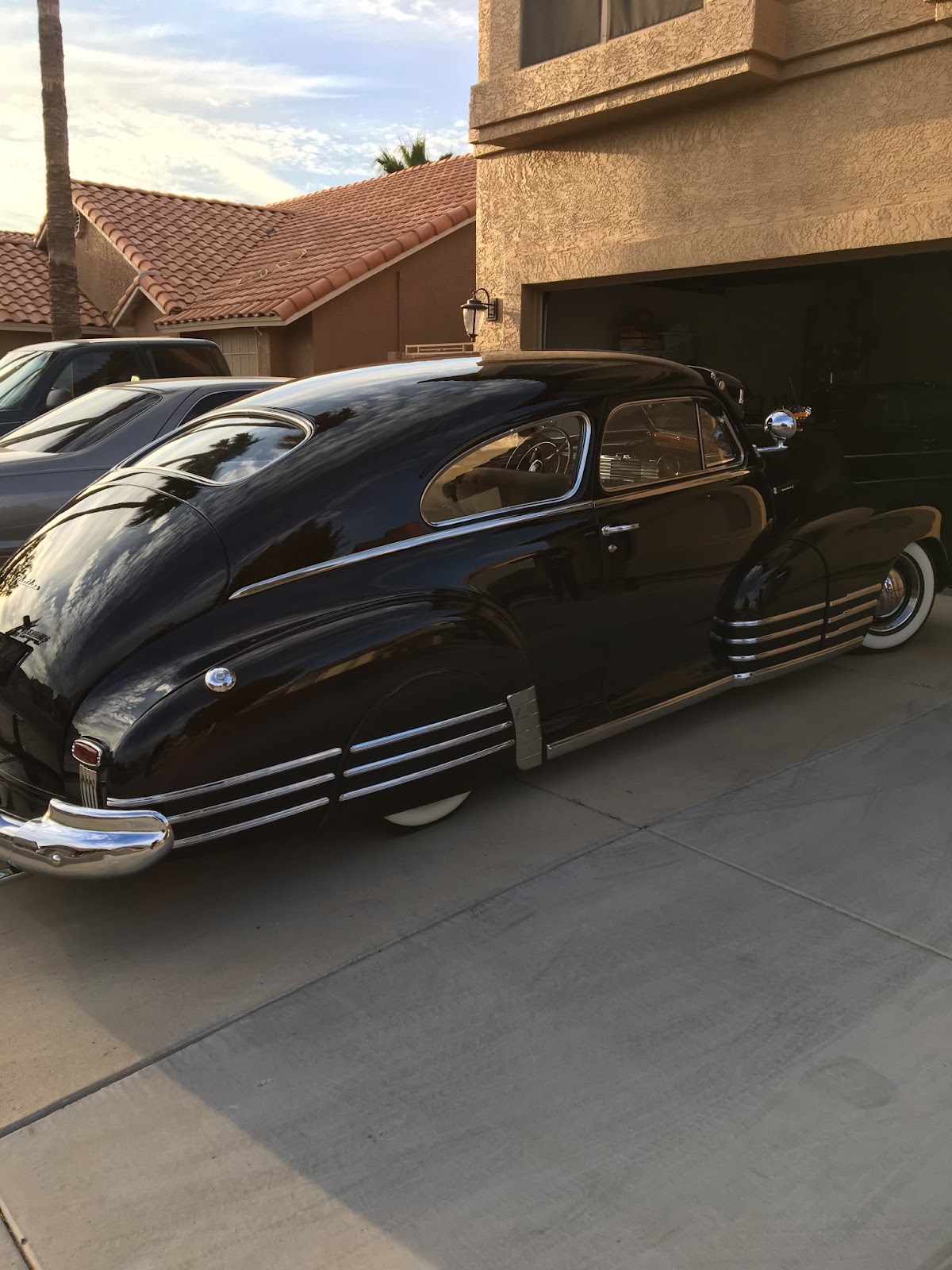 Black 1940s Chevy on whitewall tires parked in a driveway at sunset