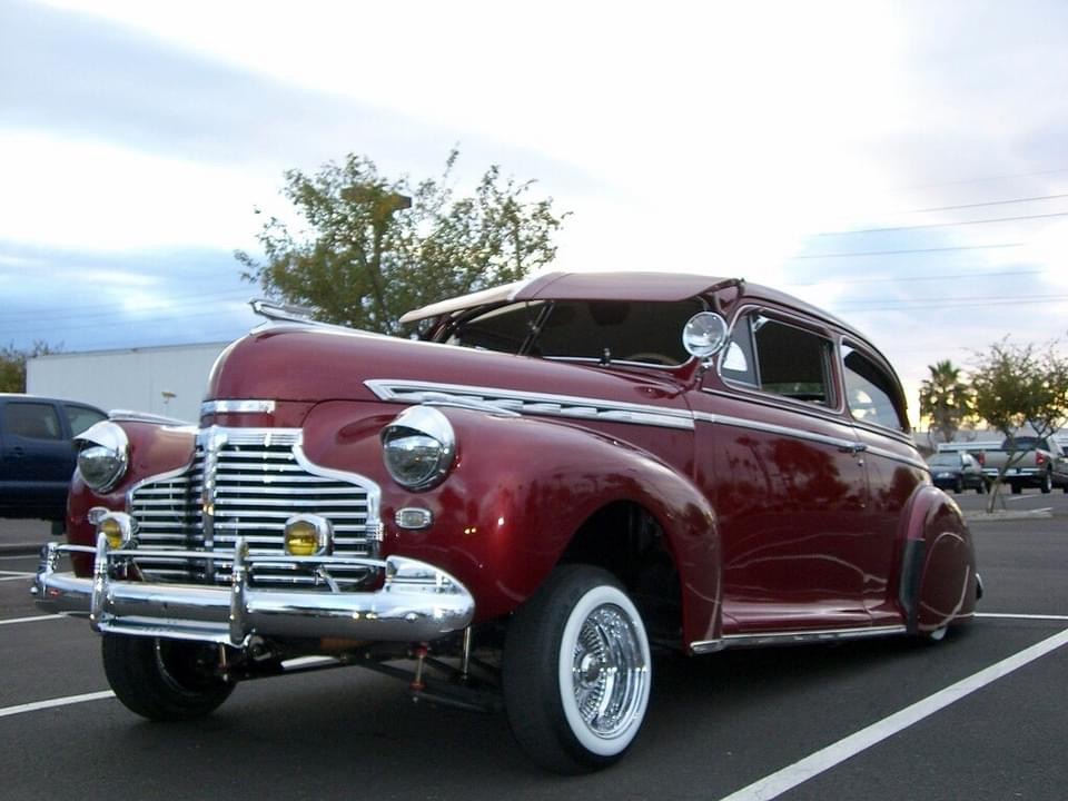 Deep red forties Chevy on whitewall tires and wire wheels in a parking lot at dusk
